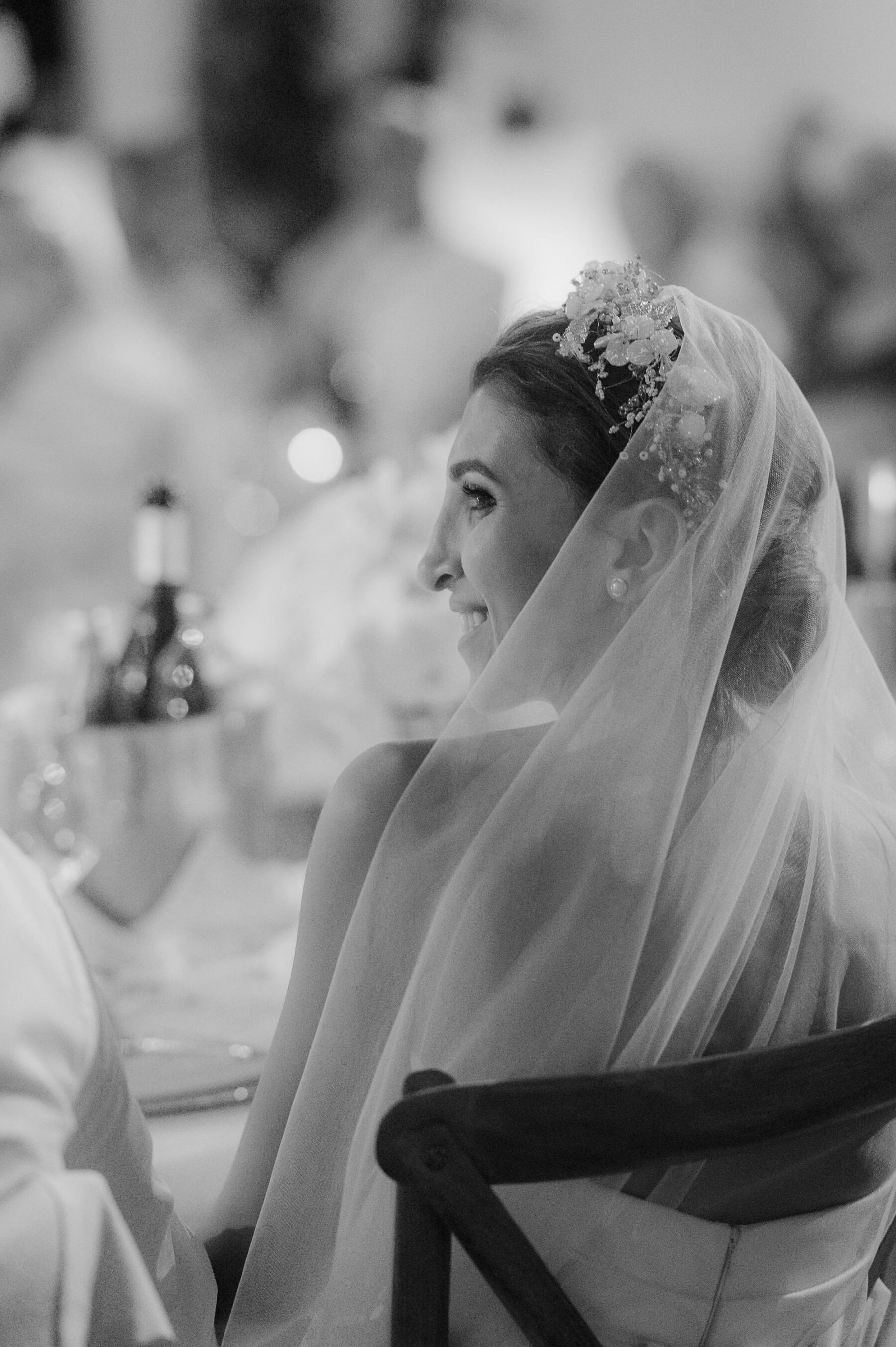 Sarah in Eva Lendel for her Classy & Contemporary Wedding in Croatia 46 Black and white profile shot of bride in a tulle veil and mother of pearl headpiece seated at the wedding reception.