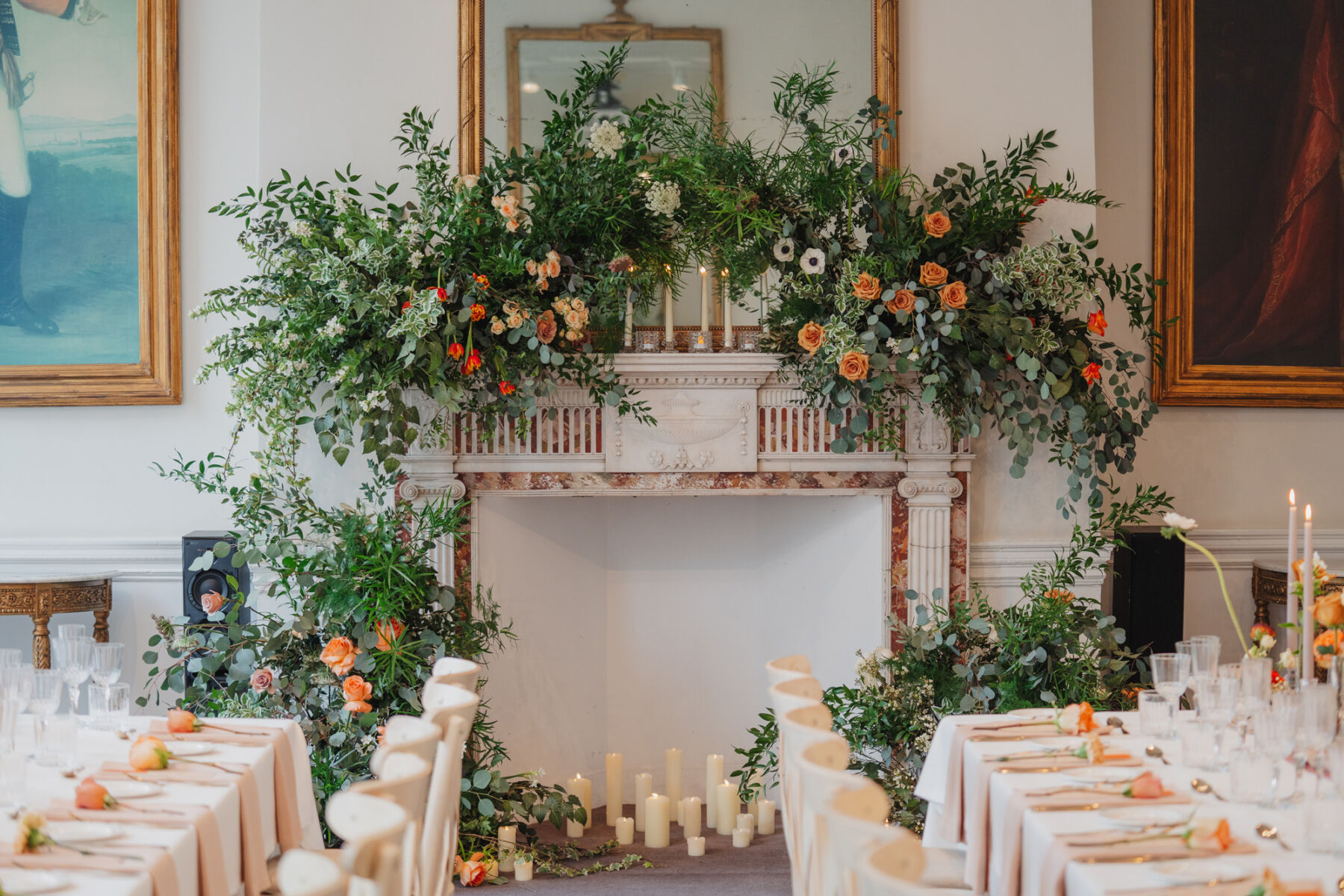 How to Create a Beautiful Sustainable Wedding on a Small Budget, with 41 Portland Place, London 8 Sprawling foliage and orange flowers decorating the fireplace and mantlepiece at 41 Portland Place London. Candles of various height sit inside the fireplace.