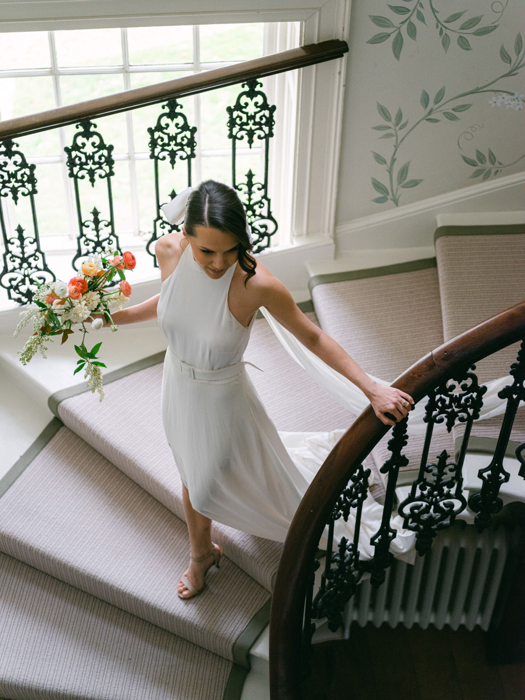 Celebrating Seasonal, British Grown Wedding Flowers With Flower & Fern at Findon Place 6 Bride descending down the staircase at Findon Place wearing an elegant halterneck wedding dress and bow-veil.
