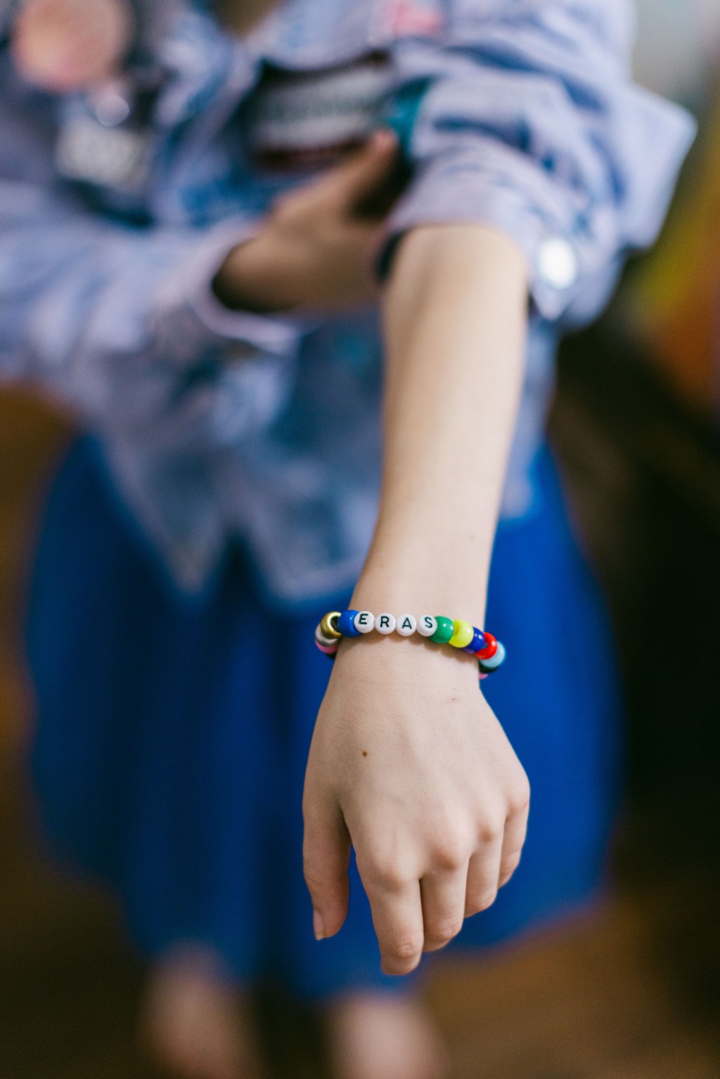 girl showing off her friendship bracelet with the word "ERAS" written on it