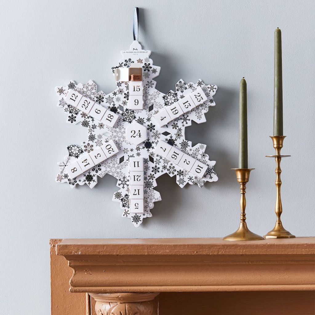 adult chocolate candy advent calendar in a snowflake shape hanging above a fireplace mantle next to two candelabras