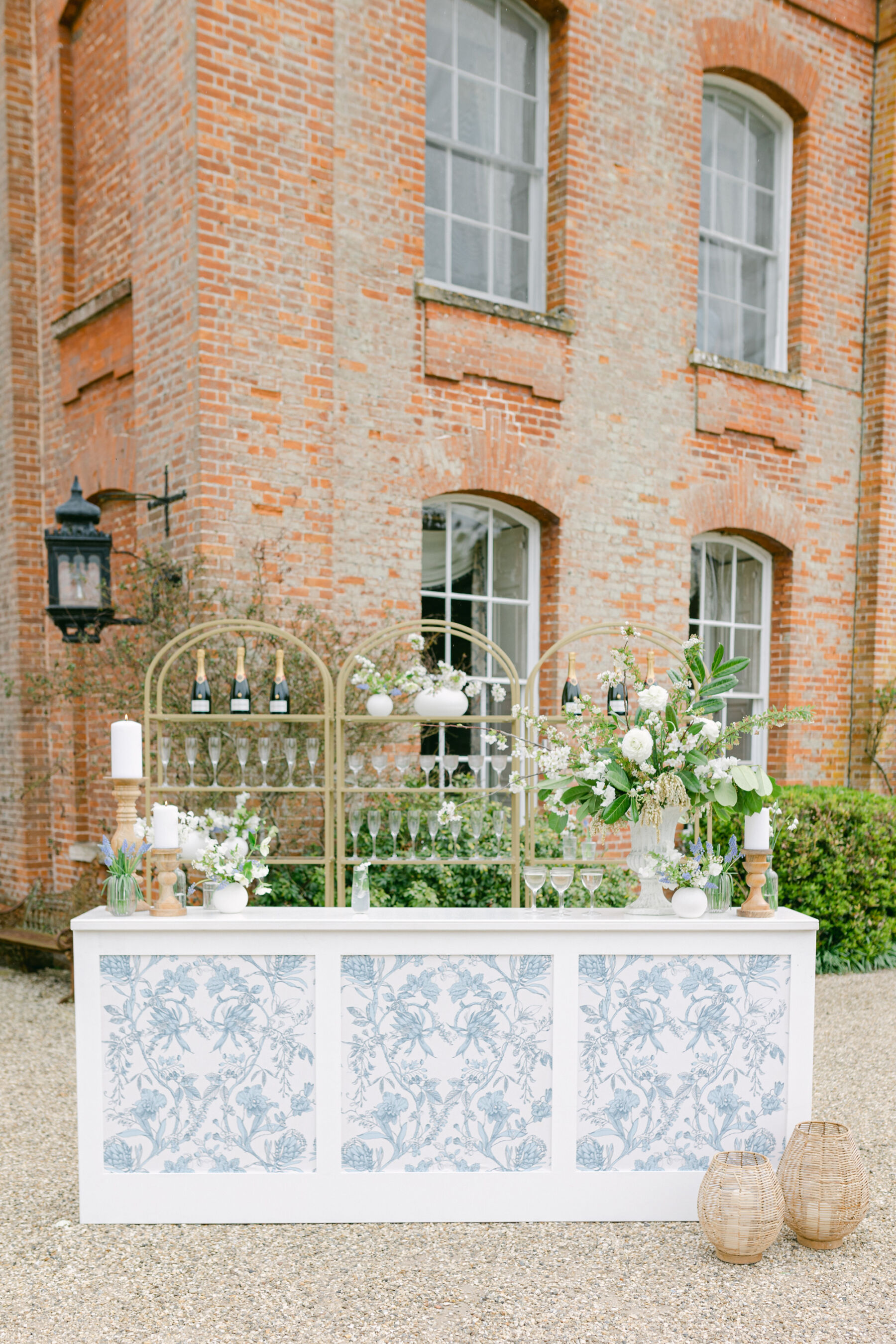 Pale Baby Blue Spring Wedding Inspiration at Avington Park, Featuring Halfpenny London 26 Elegant mobile wedding bar, with pattern blue decor, white wedding flowers and brass shelves for the bottles and glasses. White wedding flowers decorate the bar. Avington Park wedding venue, Hampshire.