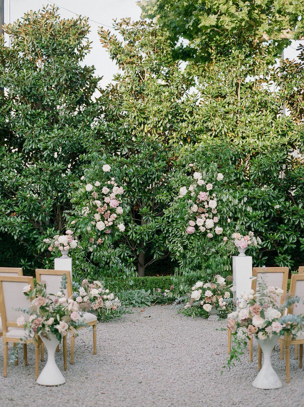 courtyard garden wedding ceremony with floral pillars and upholstered linen chairs