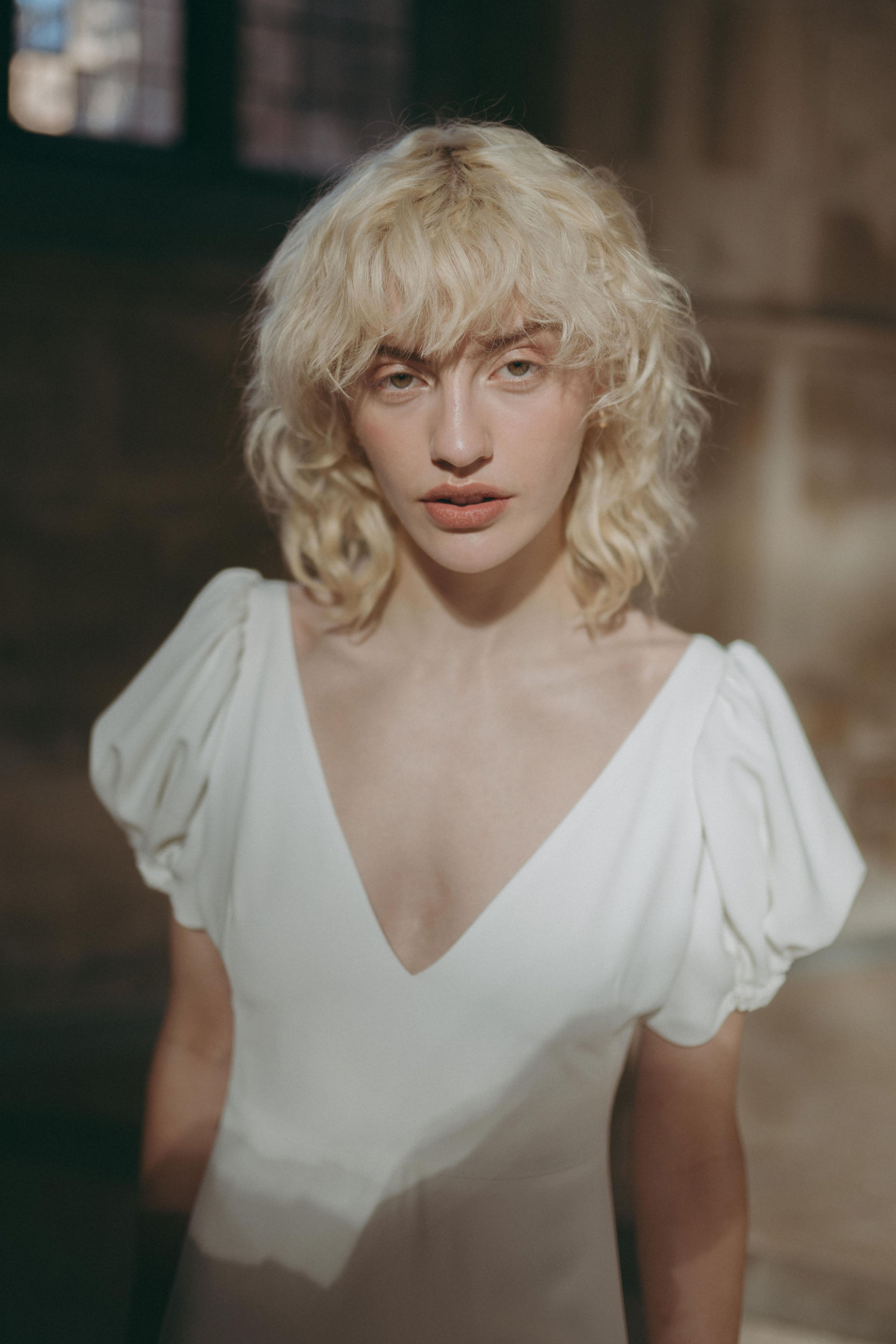 The Juliet Collection, by Rolling In Roses 17 Modern bride with choppy, wavy hair and bangs wearing a silk wedding dress by Rolling in Roses that features gently puffed/fluted sleeves.